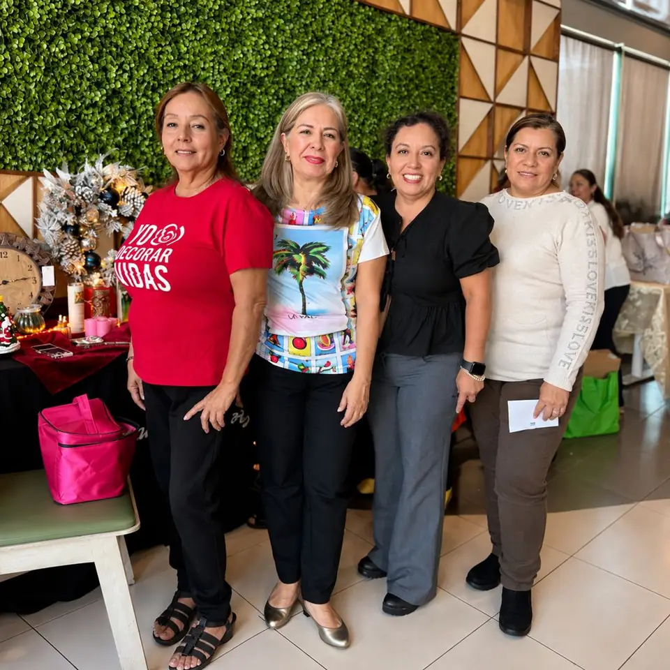Cuatro mujeres sonriendo juntas en un evento, frente a un muro verde